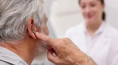 Hombre mayor con un audífono durante una consulta con una profesional