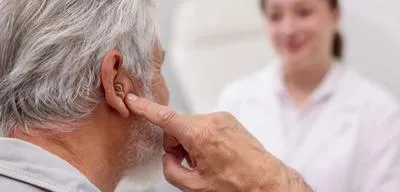 Hombre mayor con un audífono durante una consulta con una profesional